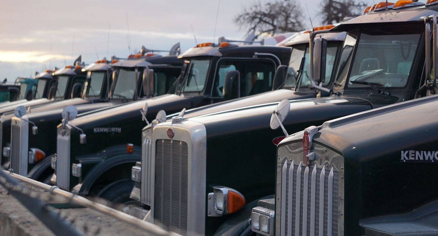 A row of conventional tractors parked nose-out under an overcast sky.