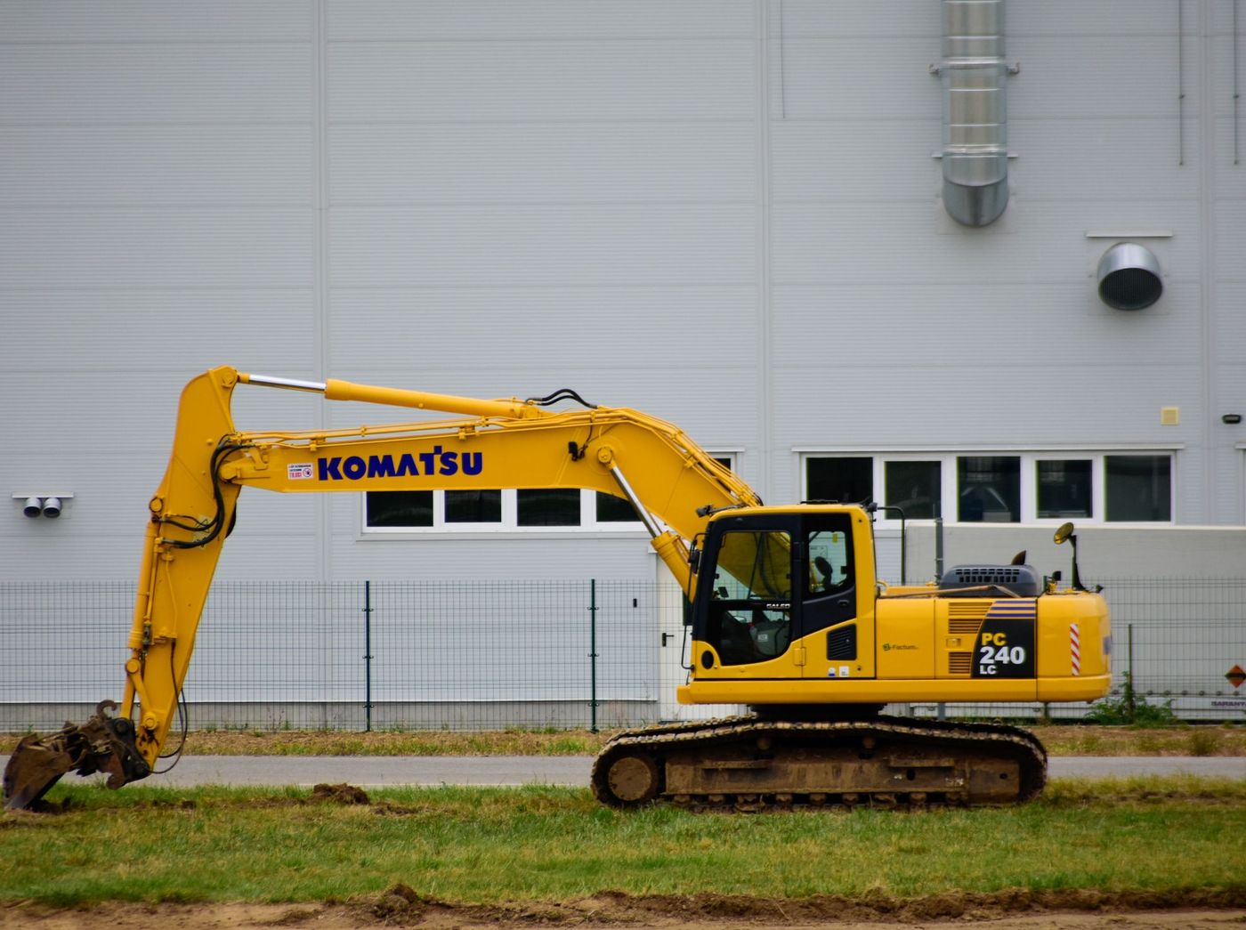 A large tracked excavator in profile, boom folded, alongside an industrial building.