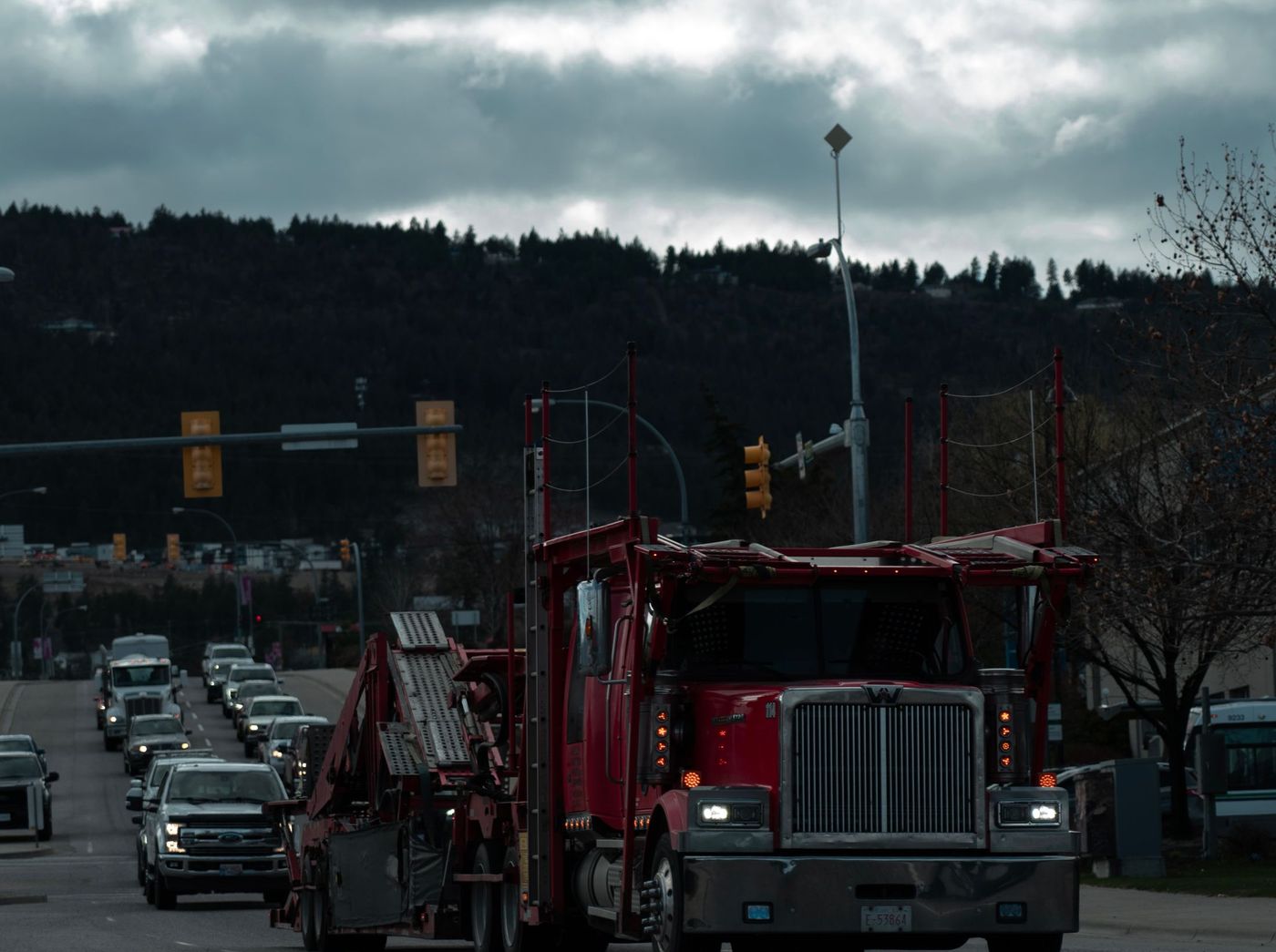 A conventional car-hauler tractor waiting at an intersection, its loading ramps folded against the rack.